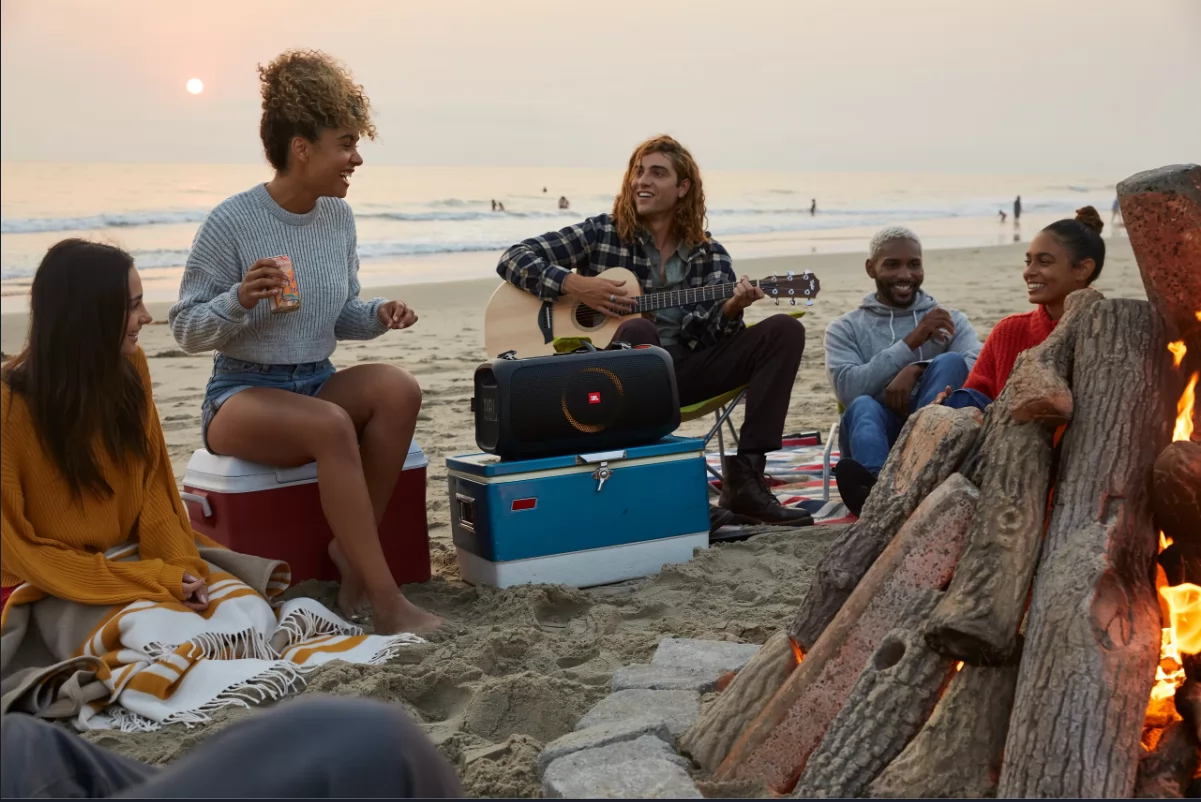 Group sitting on the beach in front of the JBL Partybox On-The-Go